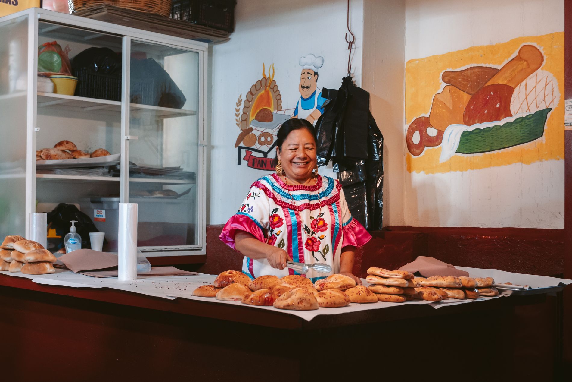 A baker smiling behind a counter full of fresh bread at her bakery