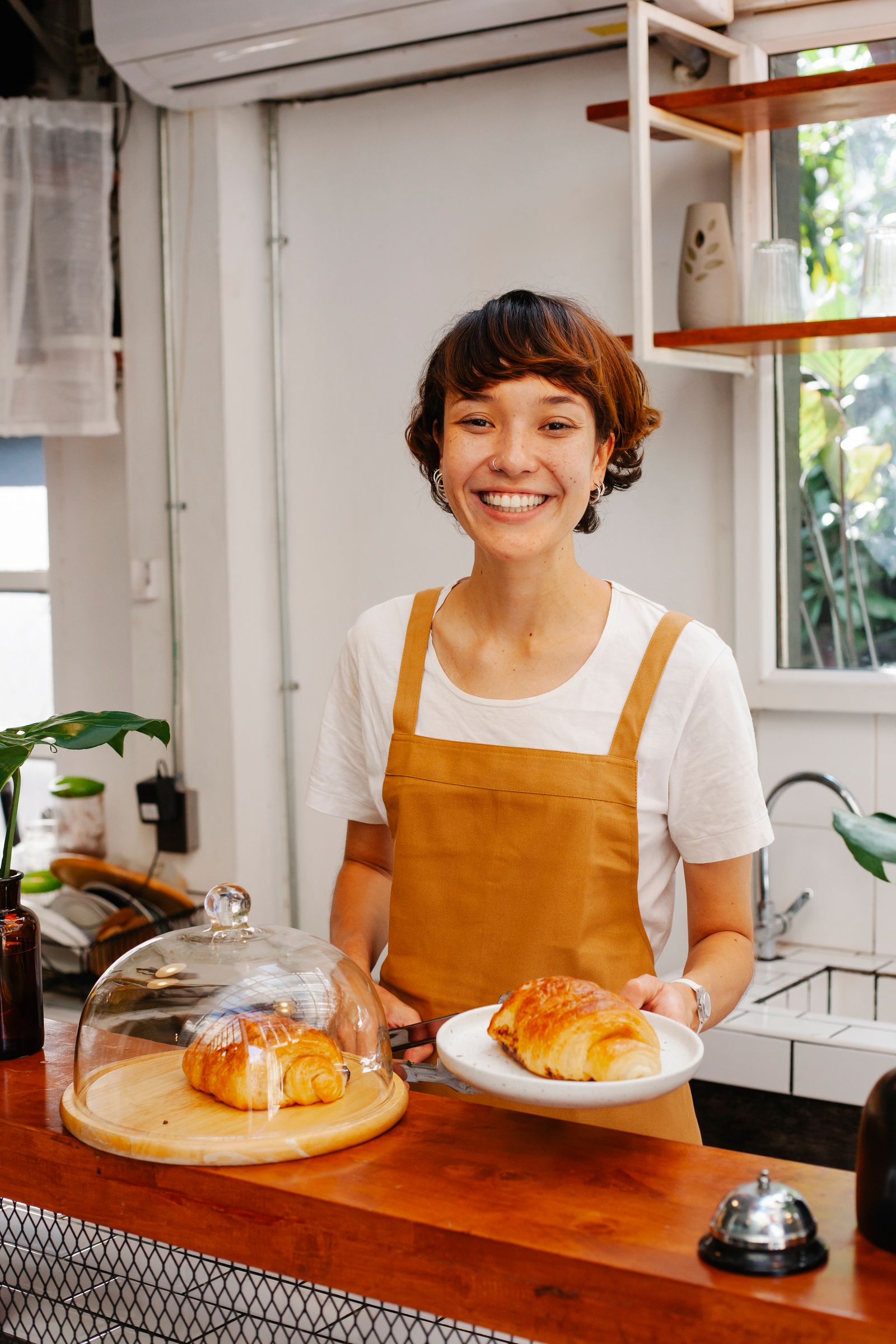 A smiling baker serving a fresh pastry at the counter of her cafe