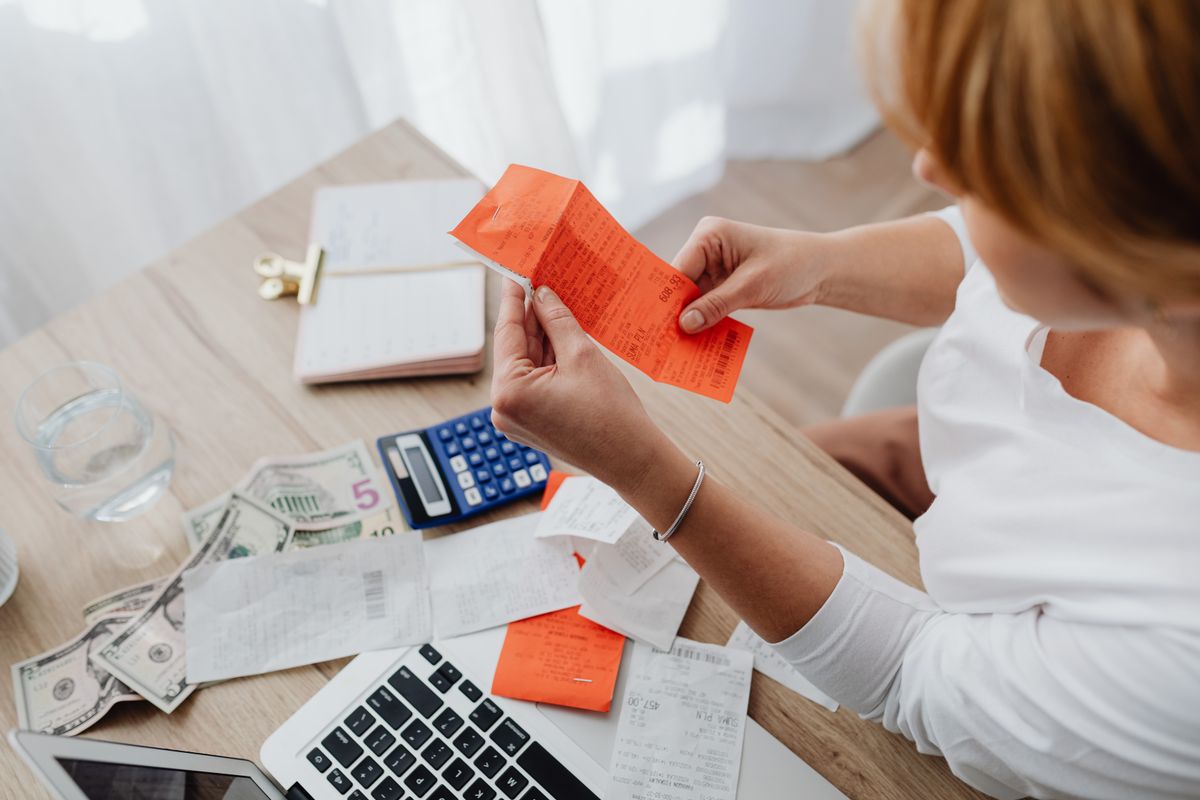A baker buried in receipts at a table, with a calculator, cash and a laptop